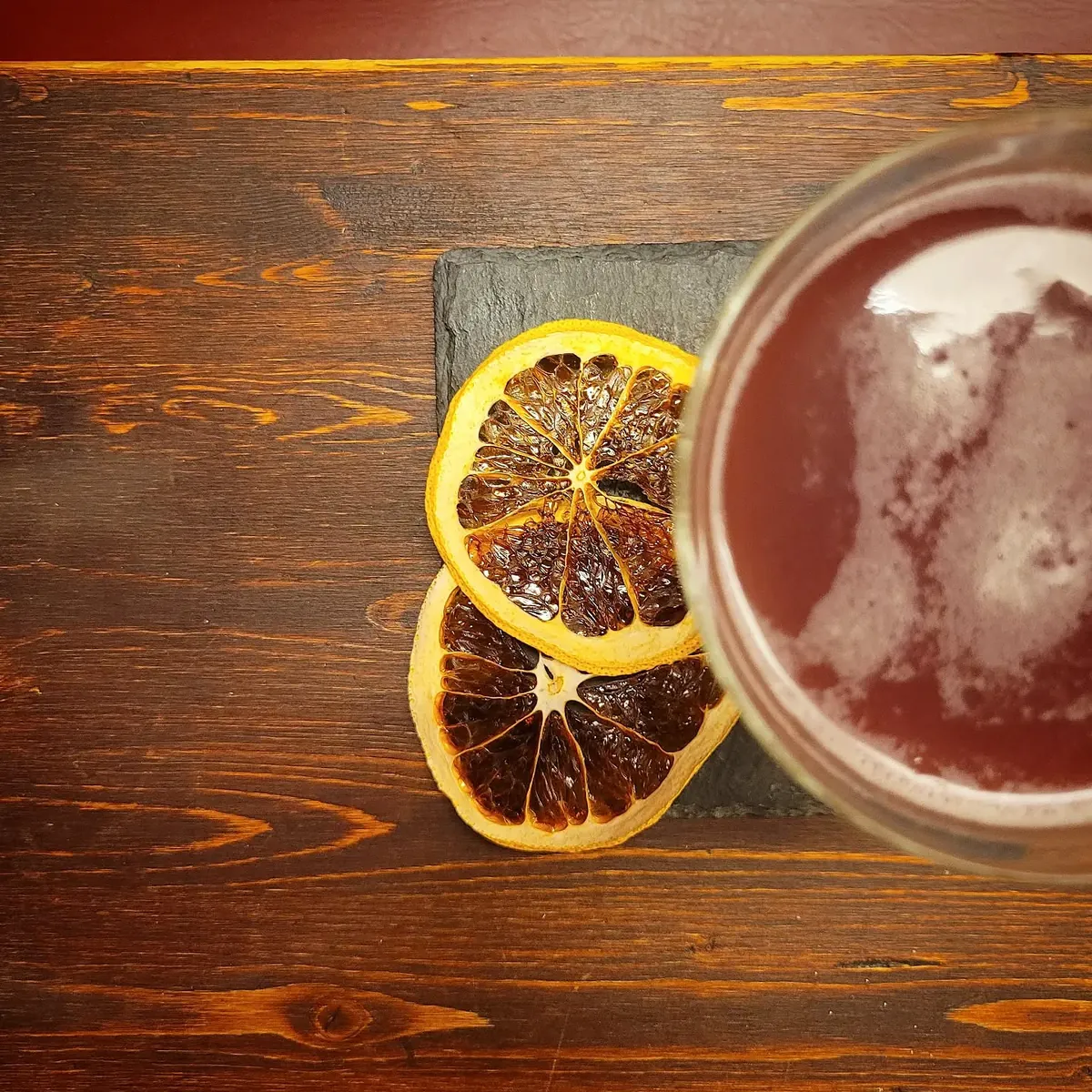 Due fette di arancia essiccata su un piattino di ardesia, accanto a un cocktail rosso scuro