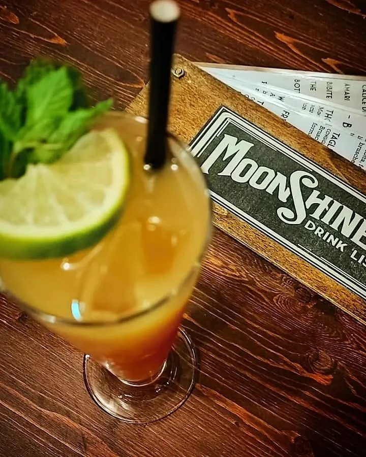 Cocktail arancione con ruota di lime e menta, accanto alla tavoletta di legno della drink list