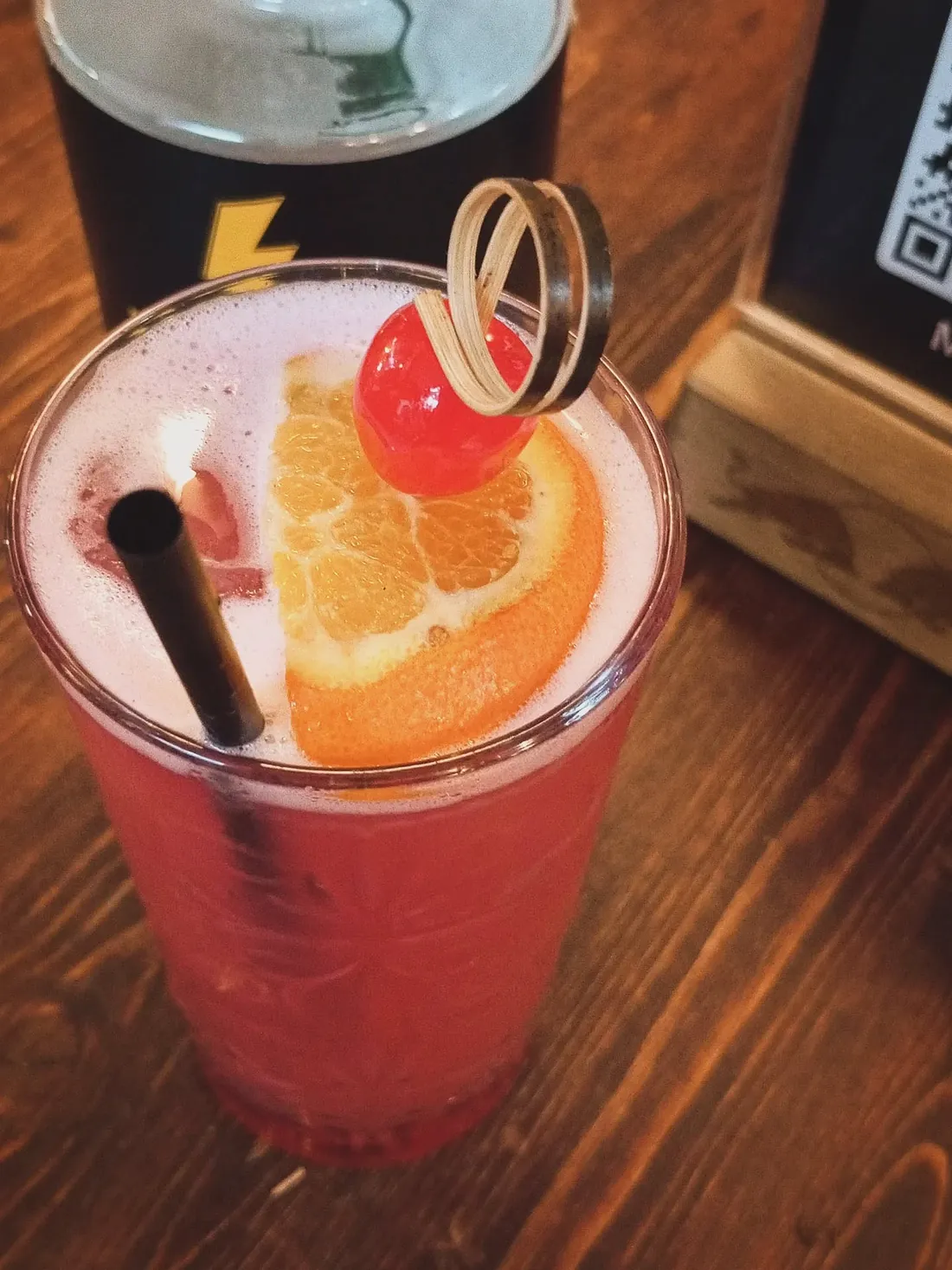 Long drink rosa con fetta d'arancia e ciliegia, in bicchiere alto lavorato