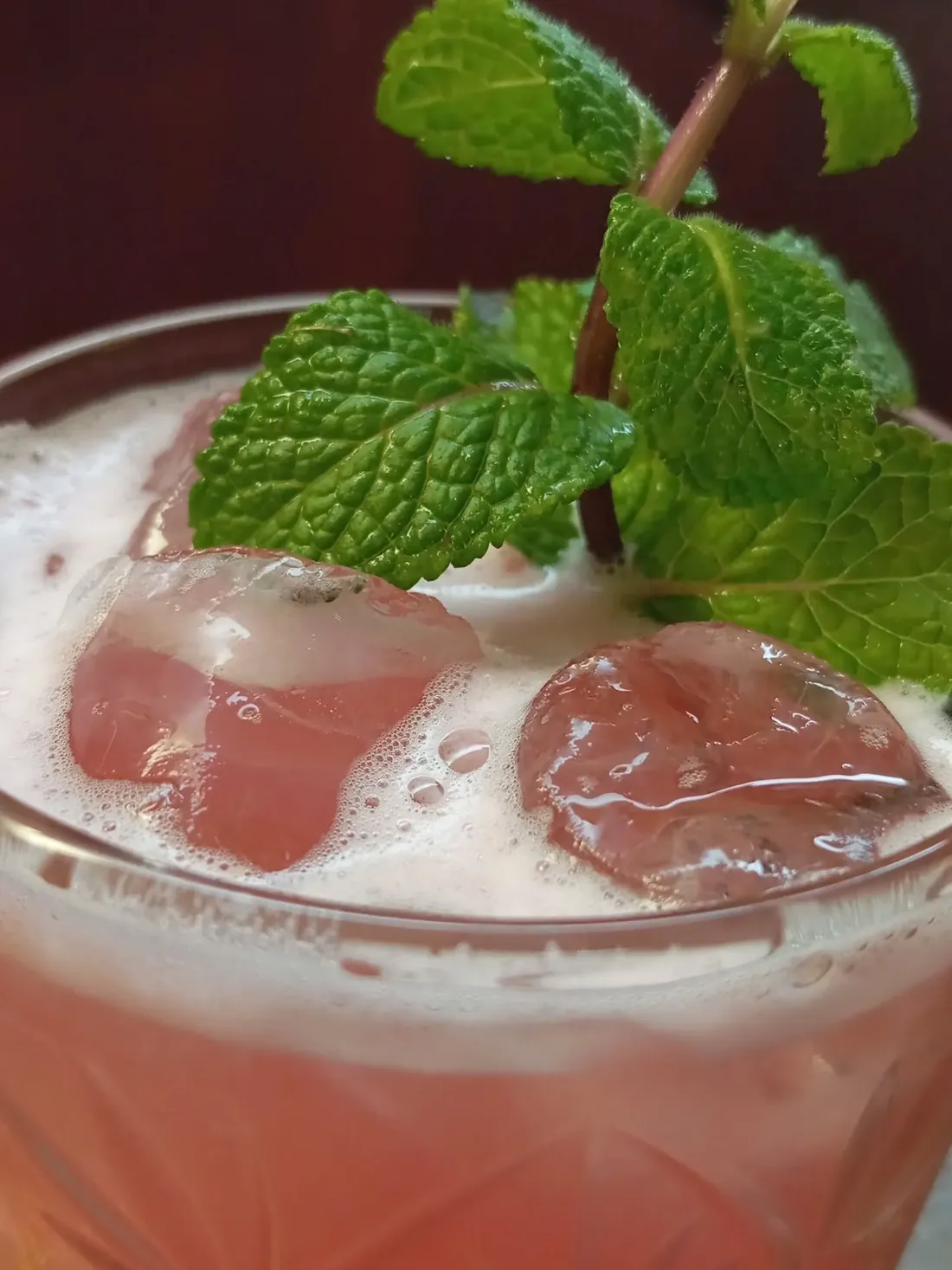 Dettaglio ravvicinato della schiuma di un cocktail rosa con ghiaccio e foglie di menta
