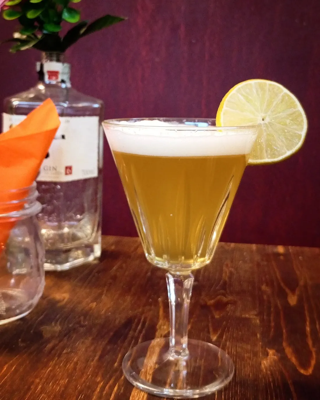 Cocktail dorato in coppa a stelo con schiuma bianca e ruota di lime
