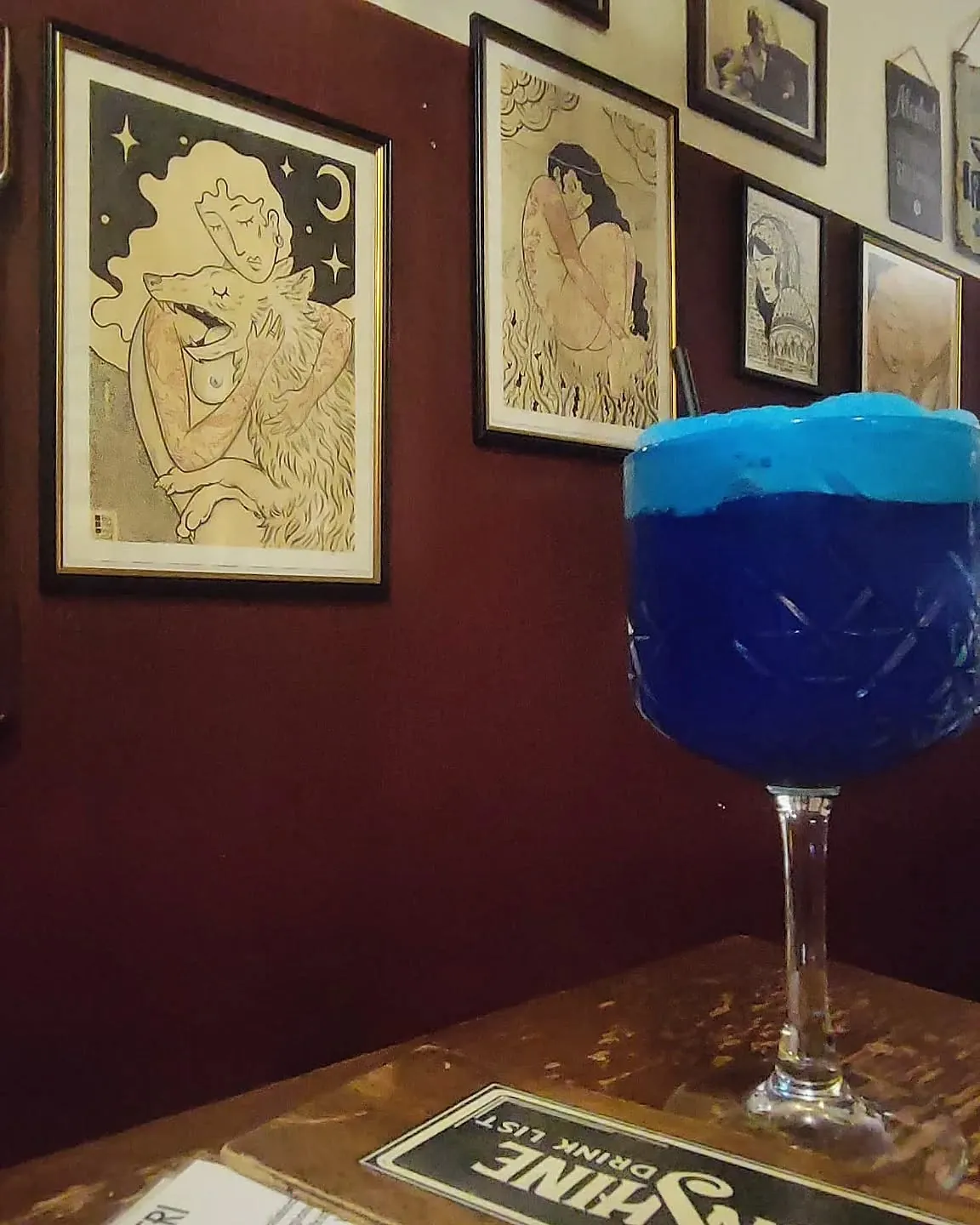 Cocktail blu in coppa davanti alla parete bordeaux coperta di stampe incorniciate