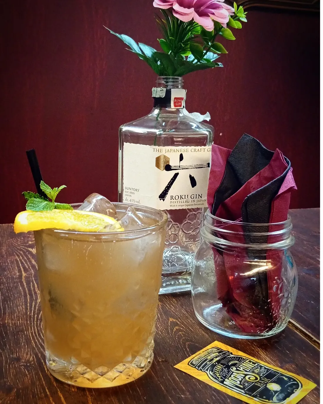 Cocktail dorato con menta e fetta di limone davanti a una bottiglia di Roku Gin giapponese